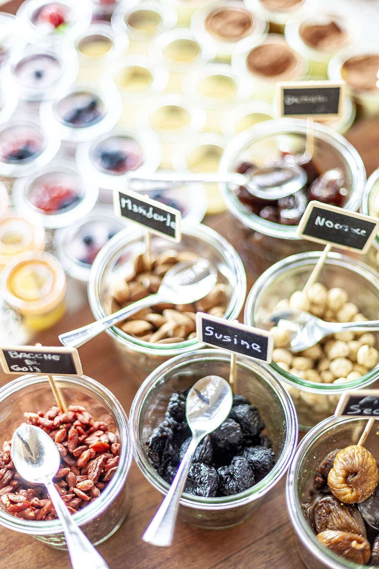 A variety of food items in glass containers with labels, including nuts, dried fruits, and other snacks.