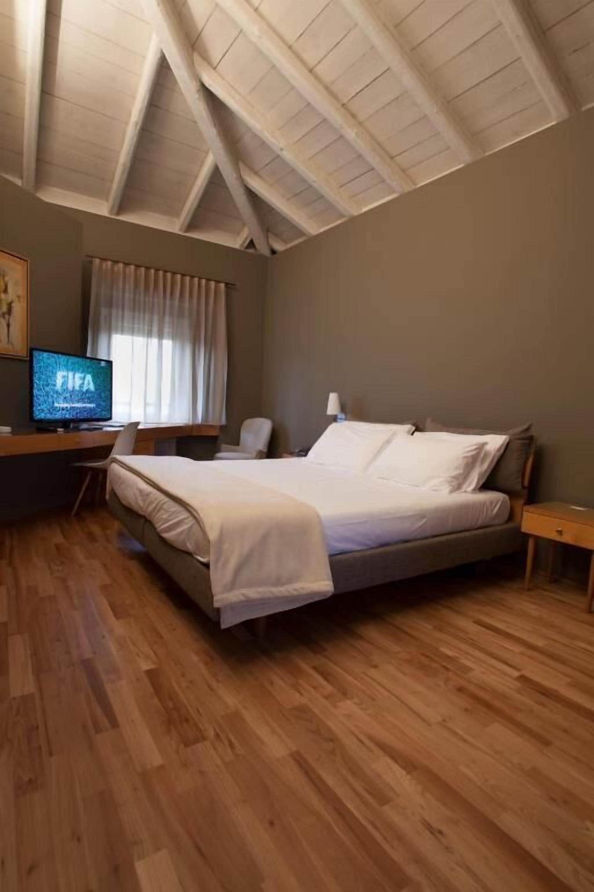 A bedroom with a bed, a desk, a chair, a TV, and a window with curtains.