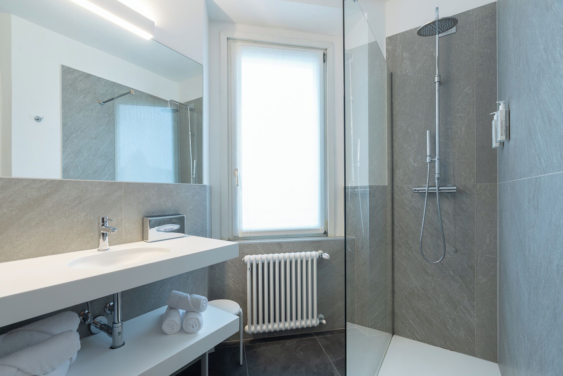 Un bagno moderno con doccia vetro, lavandino bianco e porta asciugamani.