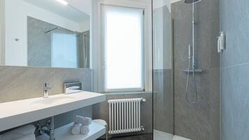 Un bagno moderno con doccia vetro, lavandino bianco e porta asciugamani.