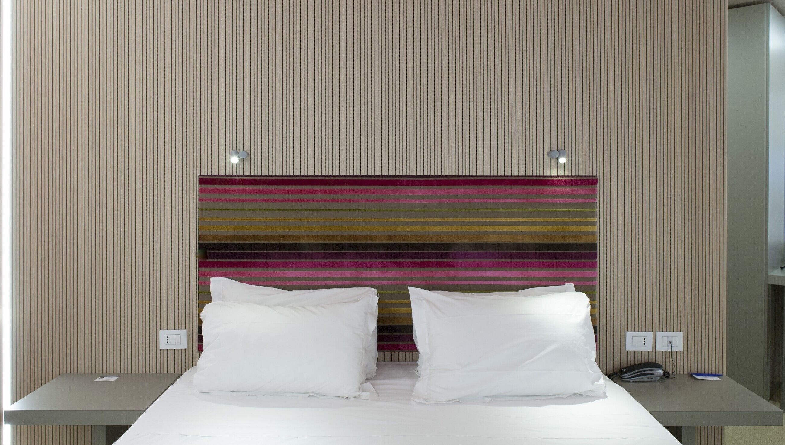 Una habitación de hotel con una cama, dos mesitas de noche y un cabecero a rayas.