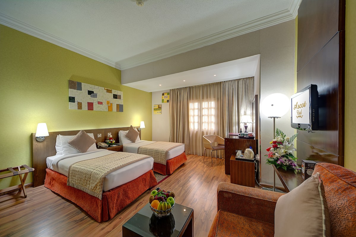 Habitación de hotel con dos camas, un escritorio, una silla, un televisor y un arreglo floral.