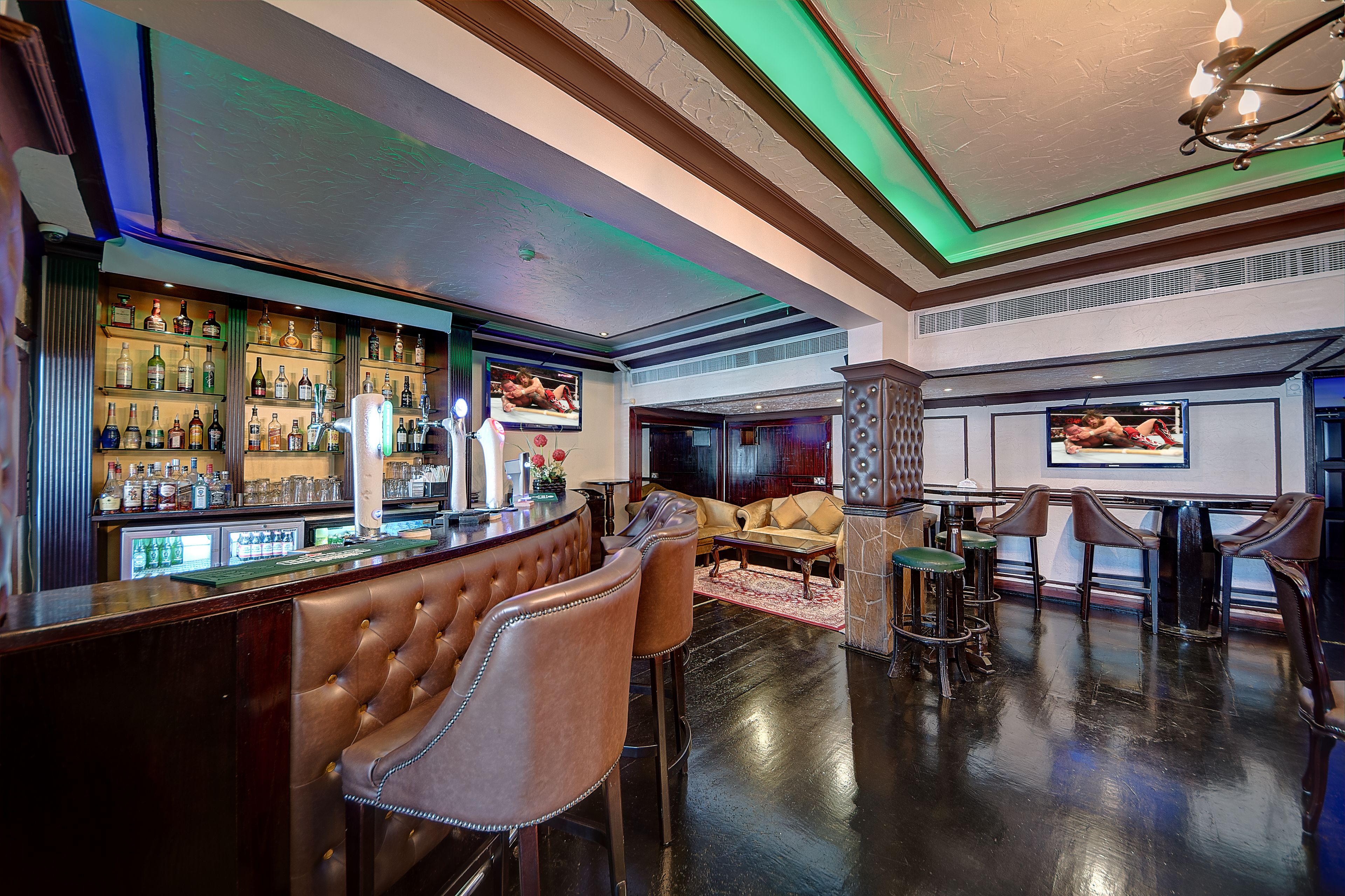 A bar area with a bar counter, multiple liquor bottles, and bar stools. There is a seating area with a sofa and chairs.