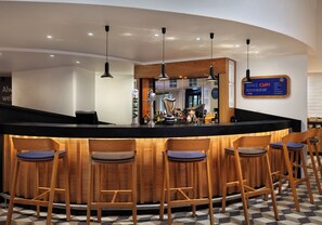 Zona de bar con mostrador curvo, taburetes de madera y una pizarra de menú.