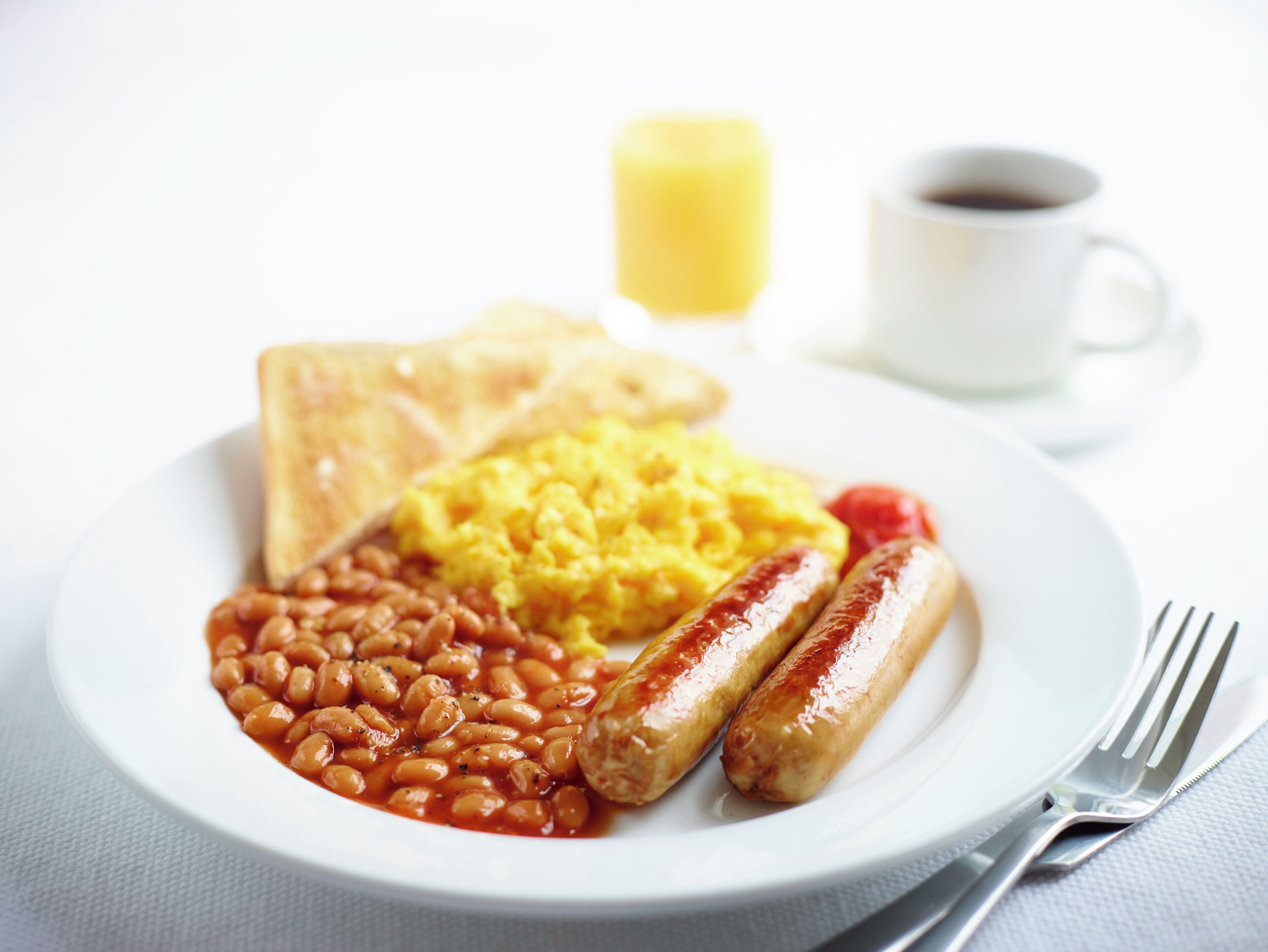 A plate with toast, scrambled eggs, beans, sausages, and a cup of coffee.