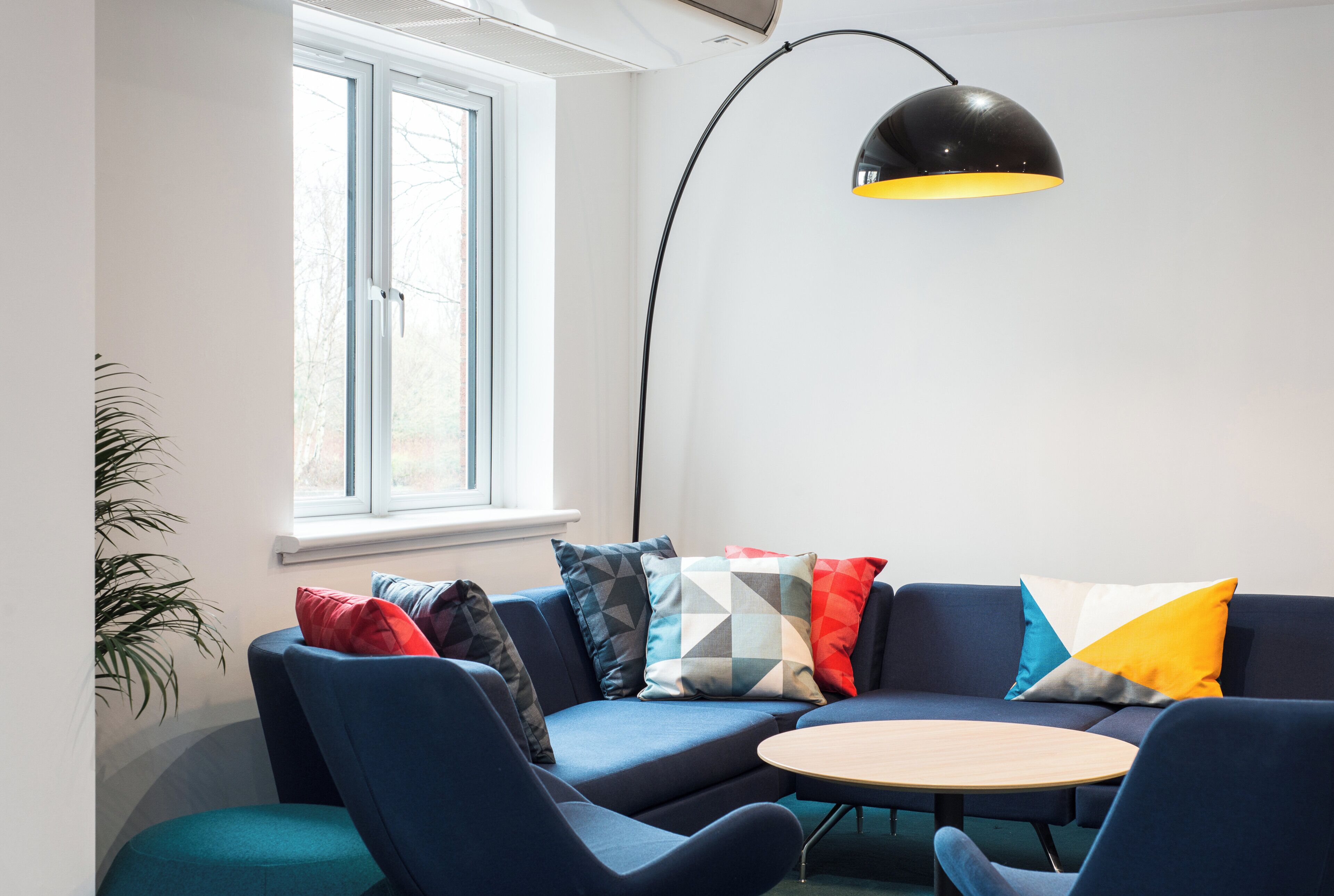 Een moderne woonkamer met een blauwe zithoek, een ronde houten salontafel en een zwarte vloerlamp.