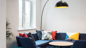 Een moderne woonkamer met een blauwe zithoek, een ronde houten salontafel en een zwarte vloerlamp.