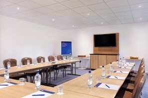 Una sala conferenze con un lungo tavolo, sedie, bottiglie d'acqua e un grande schermo.