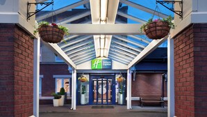 A hotel entrance with a covered walkway, a Holiday Inn Express sign, and hanging flower baskets. - Holiday Inn Express Strathclyde Park M74 JCT 5 by IHG (Glasgow)