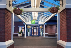 A hotel entrance with a covered walkway, a Holiday Inn Express sign, and hanging flower baskets. - Holiday Inn Express Strathclyde Park M74 JCT 5 by IHG (Glasgow)