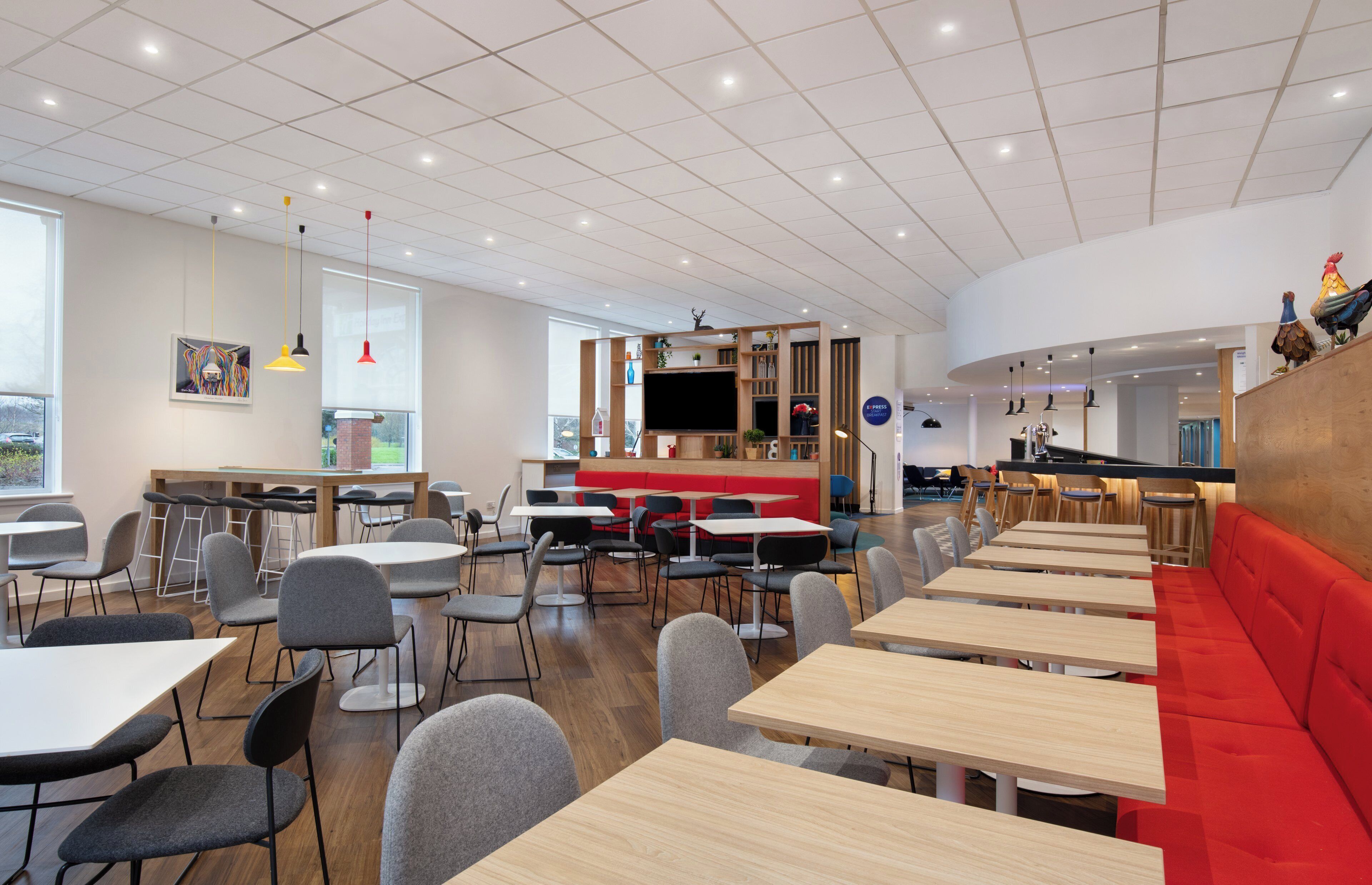 En moderne restaurant med flere siddeområder, herunder borde og båse, samt en disk til bestilling.