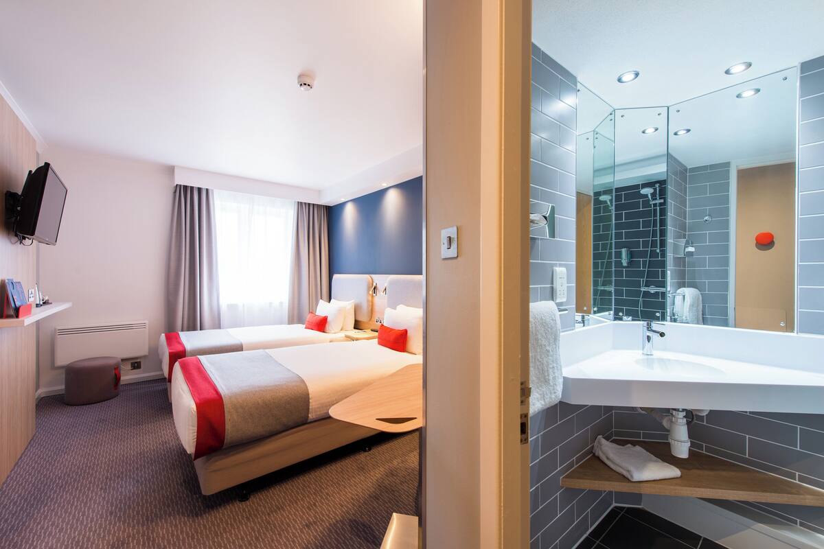 A hotel room with two beds, a TV, a large bathroom with a modern sink and mirror.