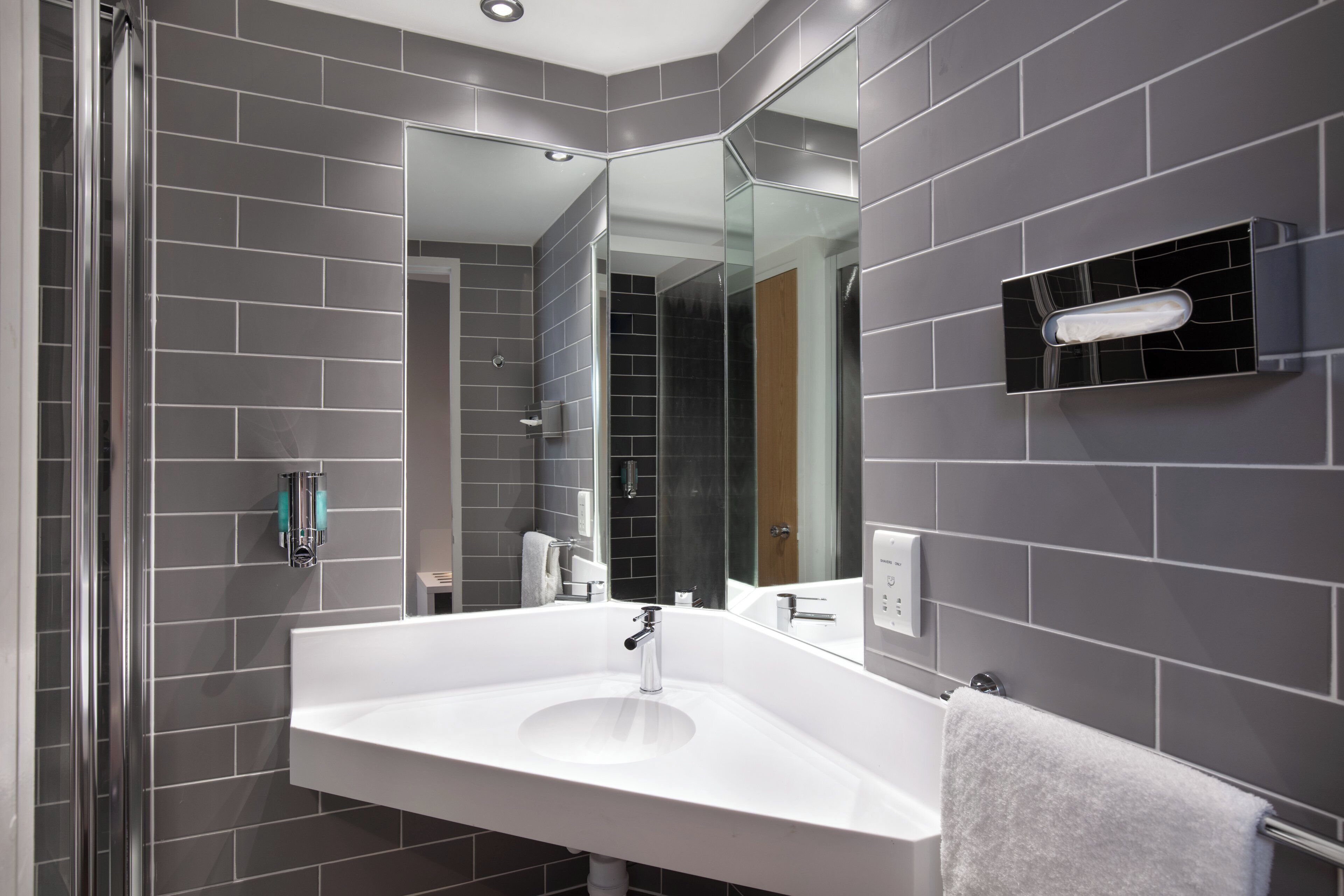 Un baño moderno con un lavamanos blanco grande, cabina de ducha de vidrio y paredes con azulejos grises.