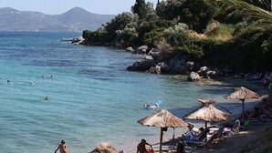 A beach with clear turquoise water, people swimming, and thatched umbrellas on the shore. - Canvas by Mitsis Belvedere (Corfu)