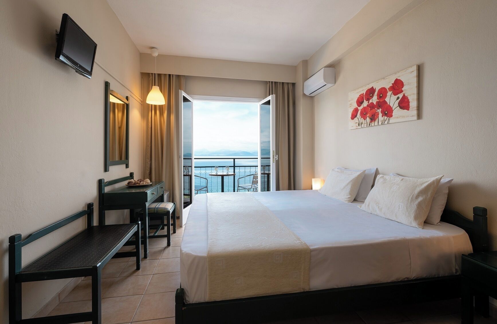 A hotel room with a bed, desk, chair, TV, artwork, and a balcony with a view.