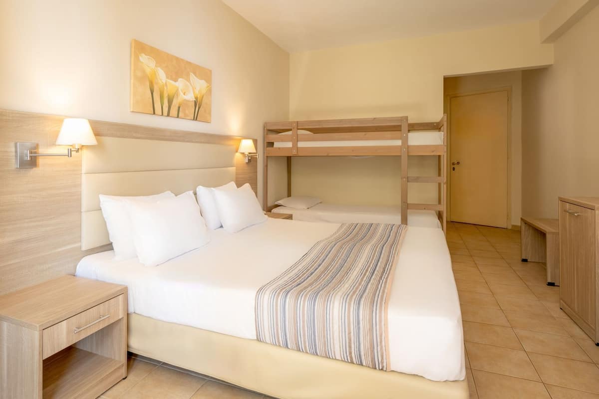 A hotel room with a bunk bed, a bedside table with a lamp, a painting on the wall, and a door.