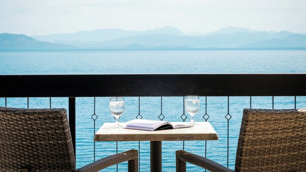 A balcony with wicker chairs, a small table, and two glasses of water. - Canvas by Mitsis Belvedere (Corfu)