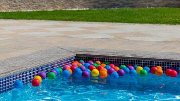Una piscina con pelotas de colores flotando y un borde con azulejos.