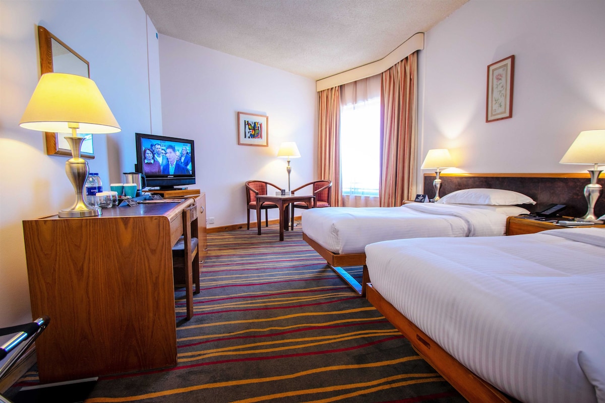 A hotel room with two beds, a desk with a television, and a chair.