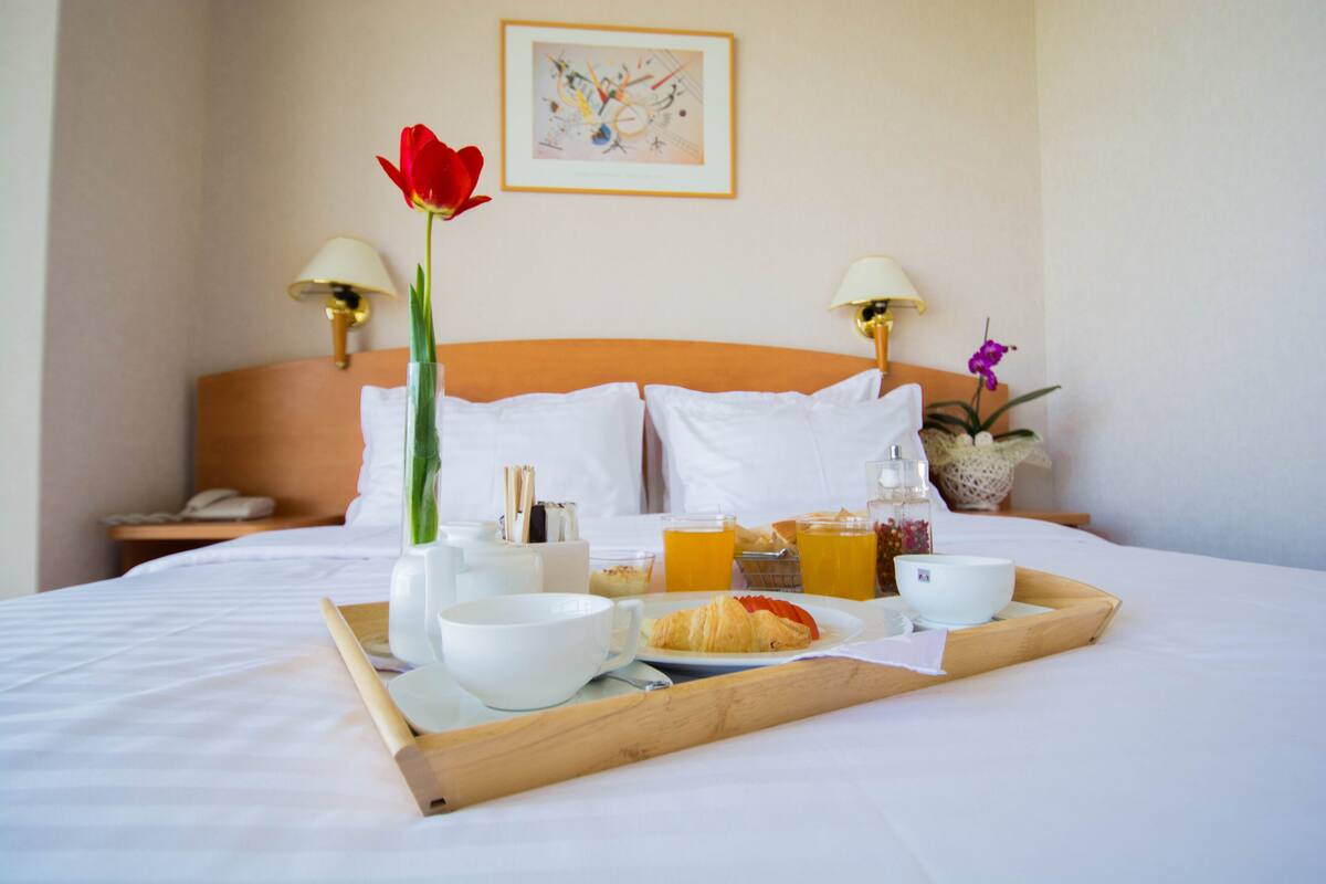 A neatly made bed with a tray of breakfast items including croissants, orange juice, and coffee.