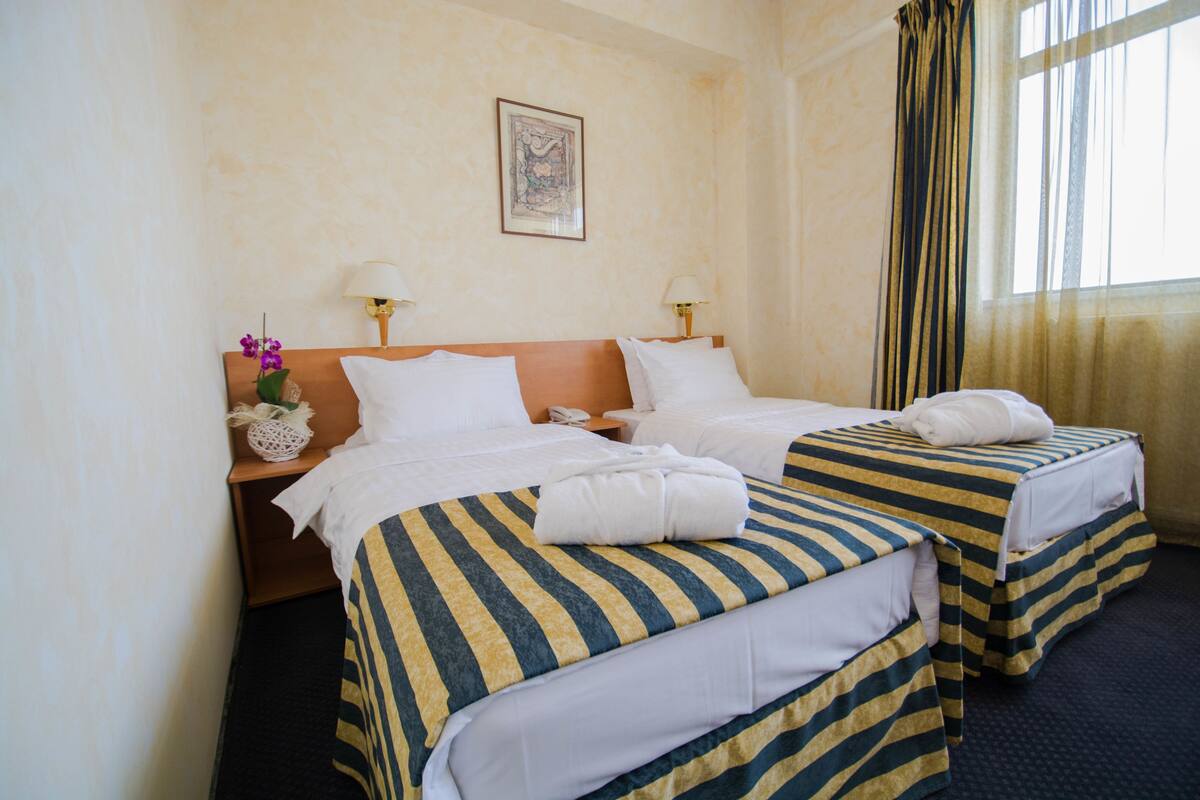A hotel room with two beds, each with striped bedding, a nightstand with a lamp, and a framed picture on the wall.