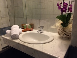 Un baño con un lavamanos blanco, un espejo y una orquídea en maceta.