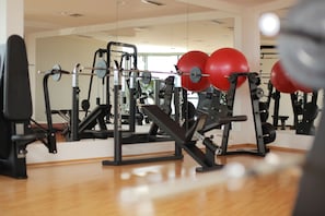 Un gimnasio con diversos equipos de ejercicio, incluyendo máquinas de pesas y balones de gimnasia rojos.