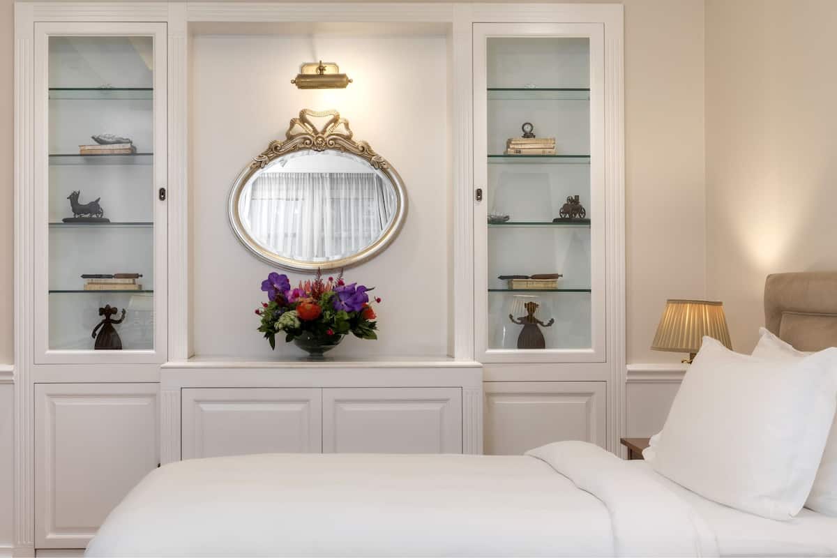 Una camera da letto con un letto, un comodino con una lampada, un settimino con ante in vetro e uno specchio sopra il settimino.