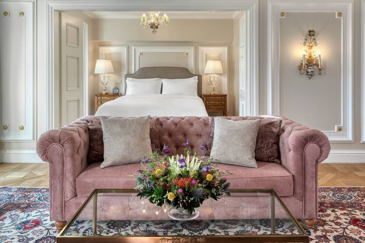 Una camera da letto con un letto grande, un divano rosa, un tavolino da caffè in vetro e un'asse di fiori.