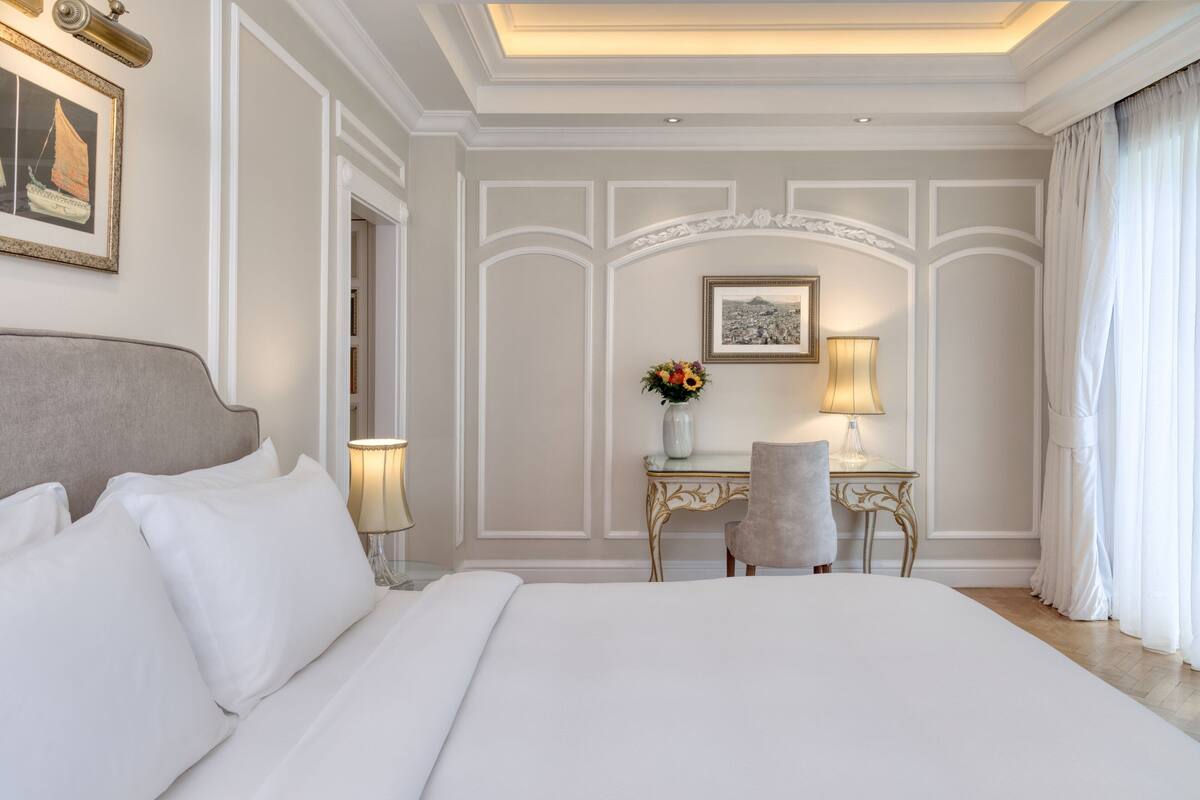 Una camera d'hotel con un letto grande, una scrivania con una lampada, un vaso con fiori e un quadro appeso al muro.