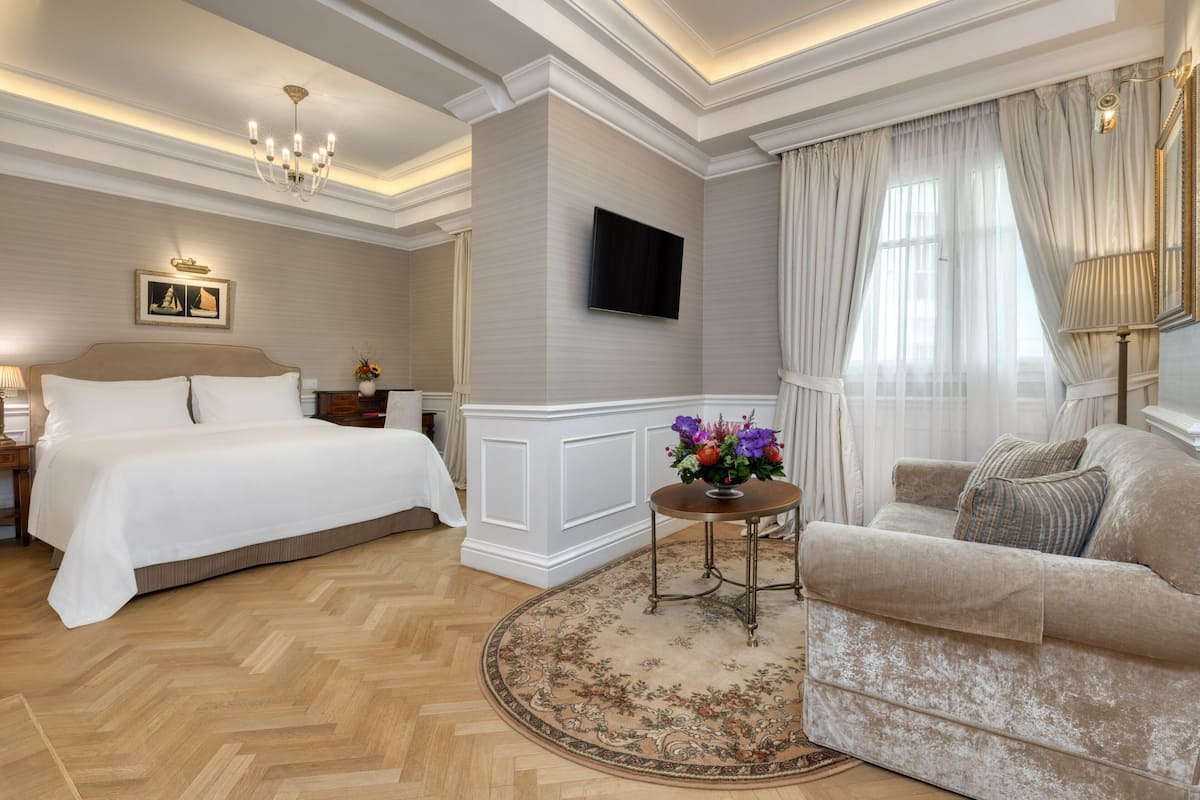 Una camera d'albergo con un letto grande, un divano, una televisione a parete e un lampadario.