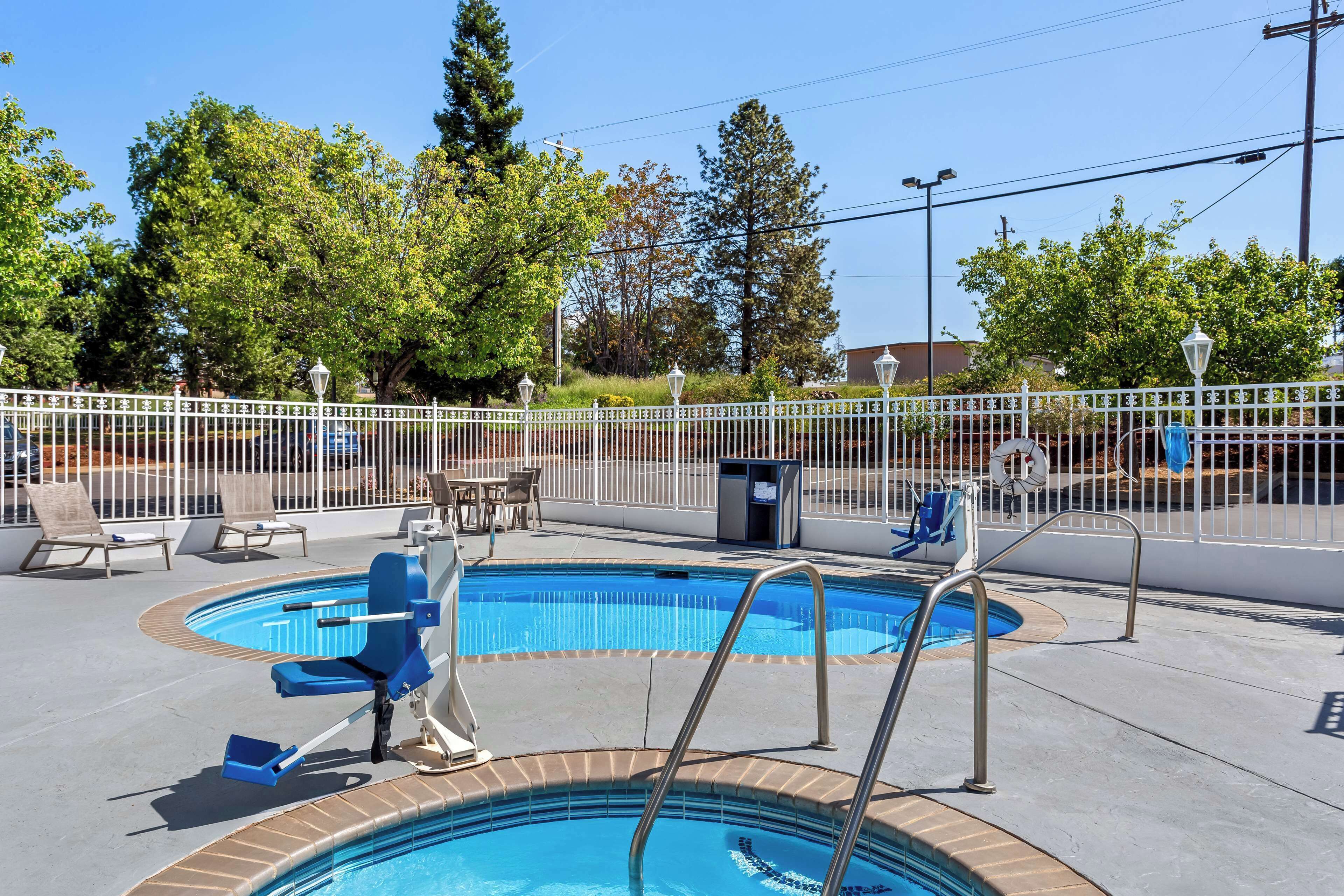 A swimming pool with a white fence, lounge chairs, and a lifeguard chair.