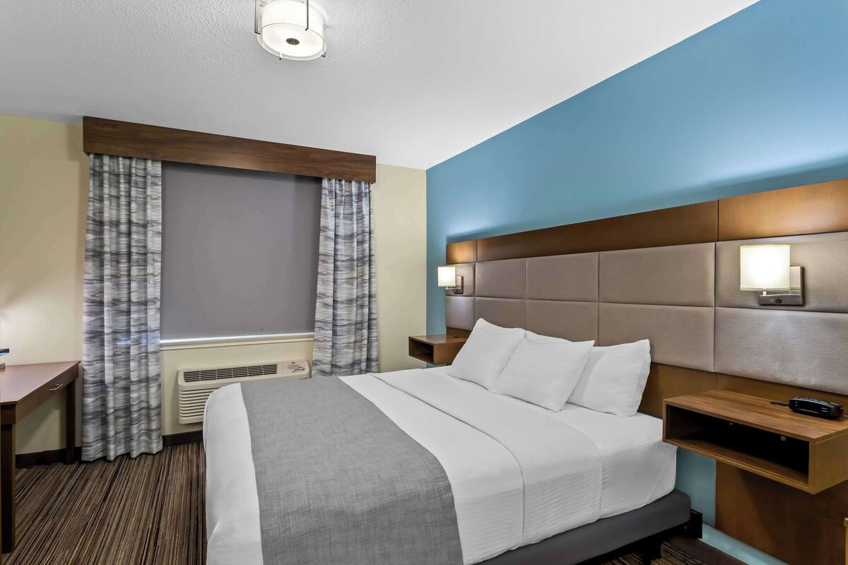A hotel room with a large bed, a nightstand, a desk, and a window with curtains.