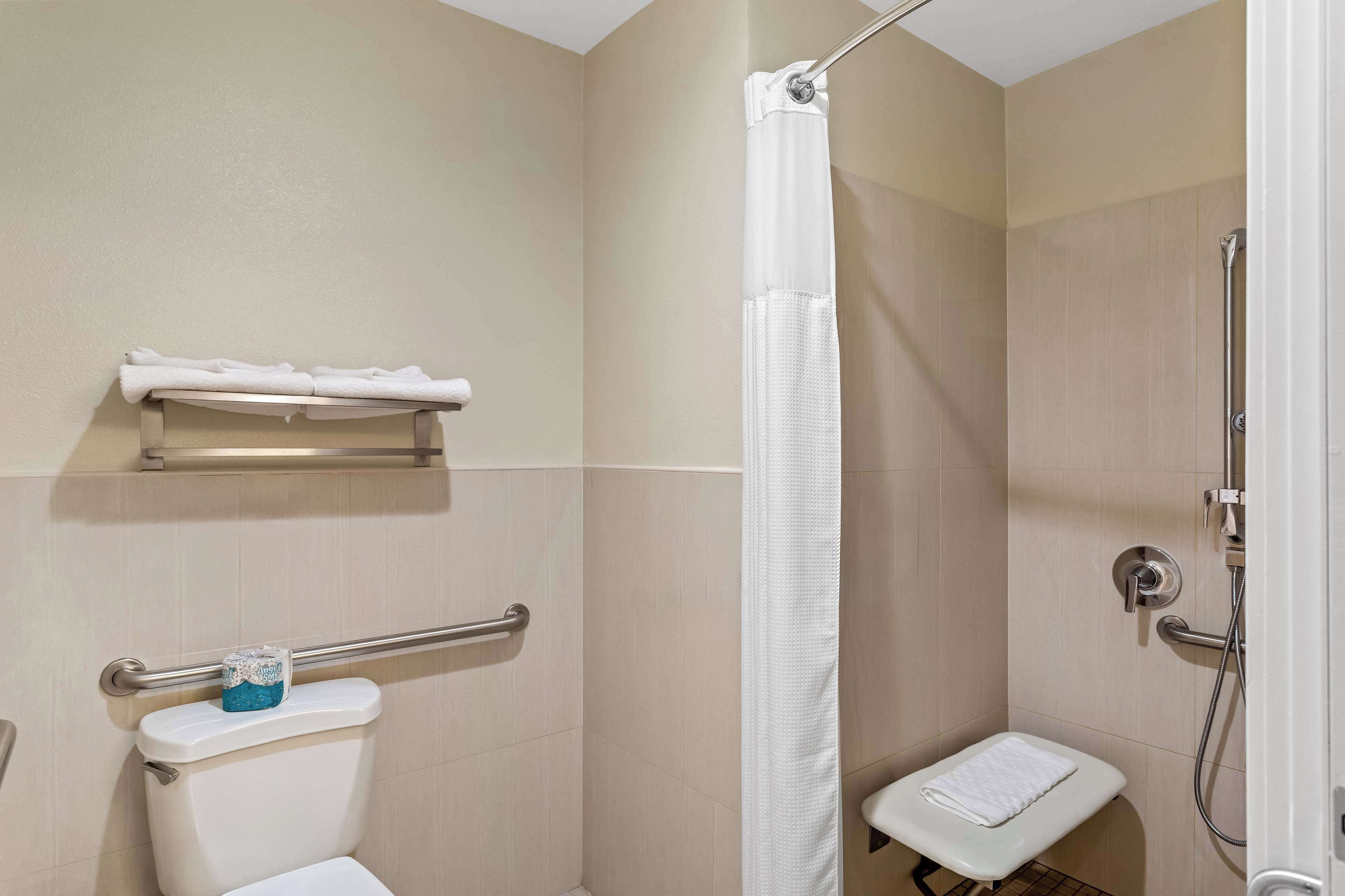 Ein kleines, privates Badezimmer mit Toilette, einer Dusche mit weißem Vorhang, einer Haltestange und einem Ablagefach mit Handtüchern.