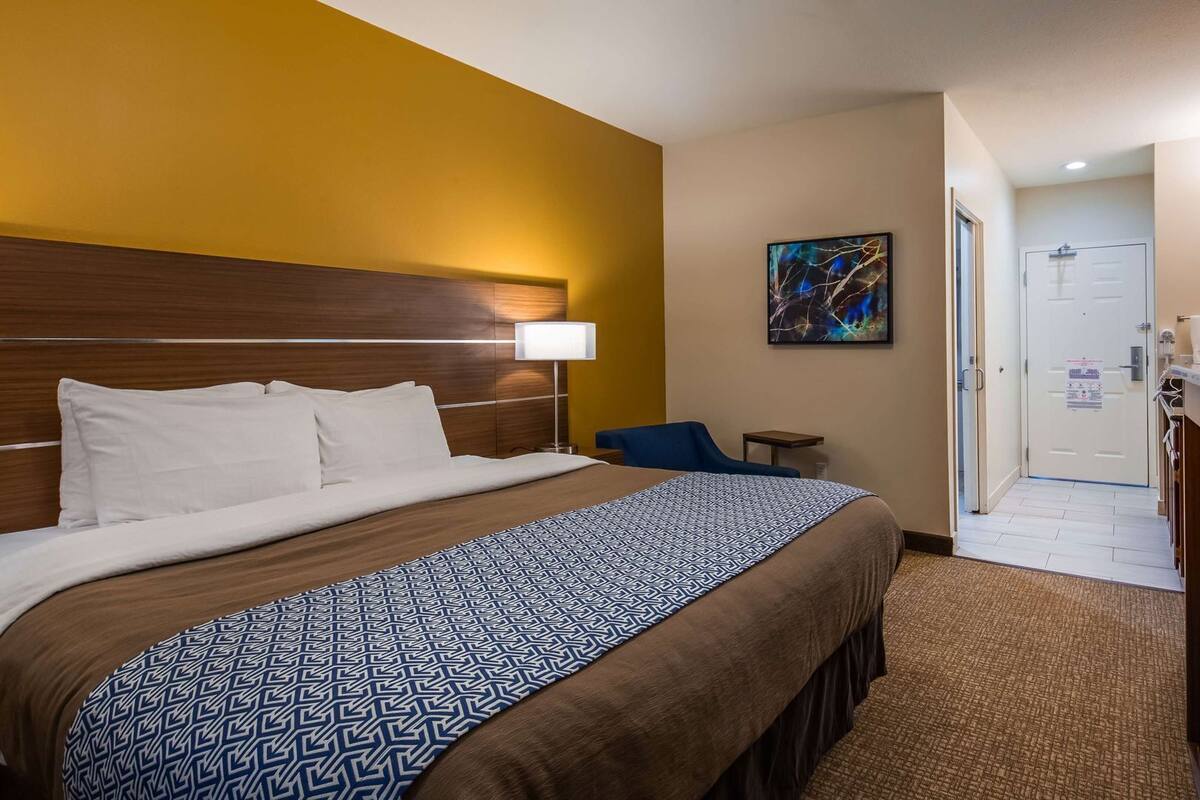 A hotel room with a large bed, a desk, a chair, a television, and a bathroom visible through an open door.