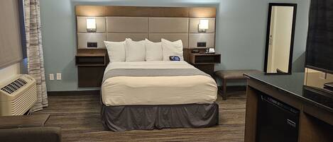 Una habitación de hotel con una cama grande, mesitas de noche, un escritorio, un espejo y un aire acondicionado integrado.