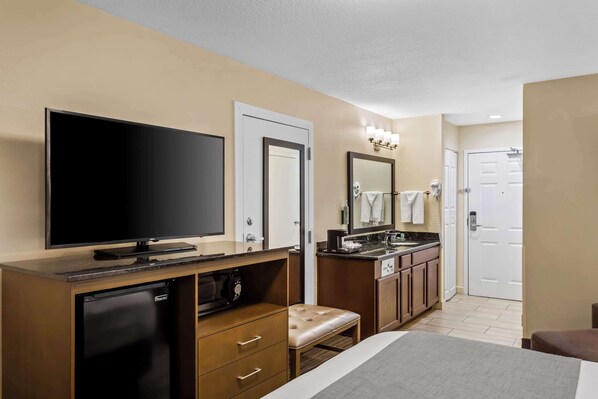 A hotel room with a flat-screen TV, a mini-fridge, a microwave, a vanity with a mirror, a sink, and a bench. - Best Western Paradise Hotel (Paradise)