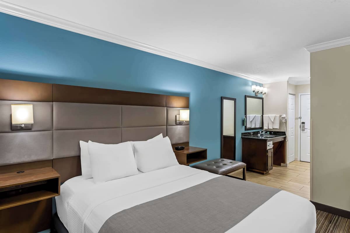 A hotel room with a large bed, a nightstand, a bench, a dresser, and a mirror.