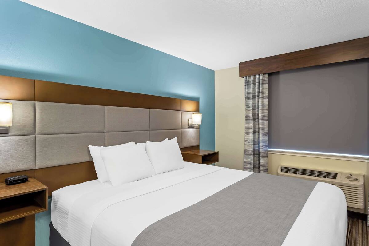 A hotel room with a large bed, a headboard, a nightstand, a lamp, and a window with curtains.