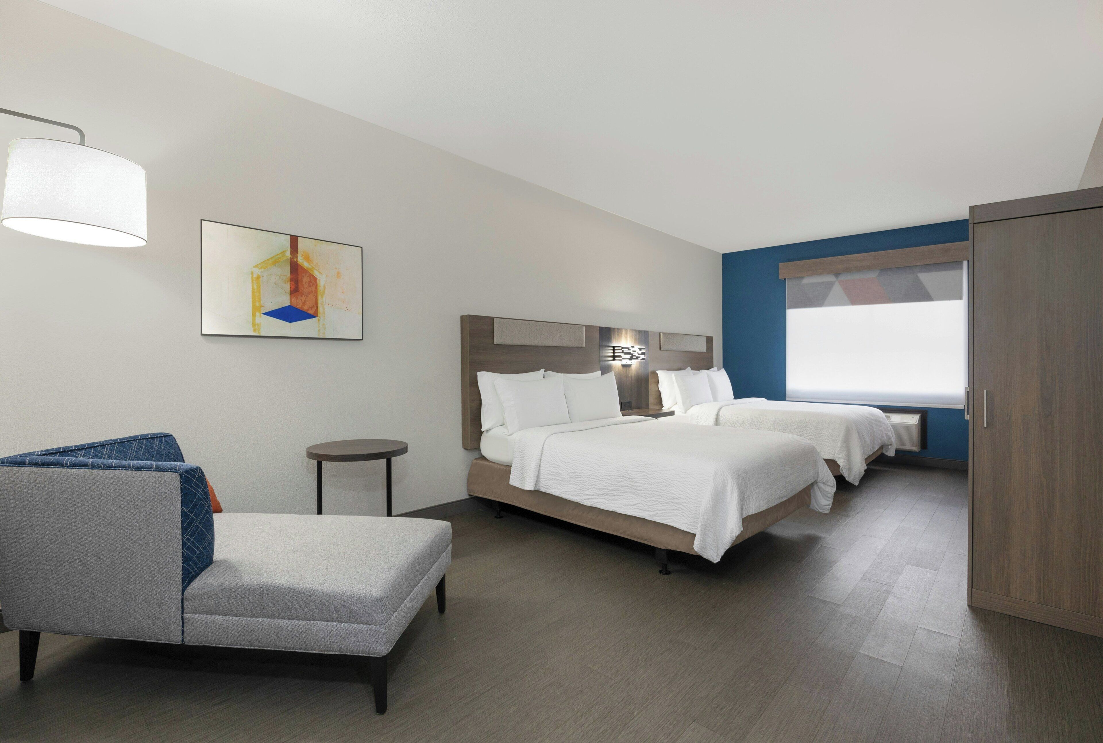 Habitación de hotel con cama, una silla, una mesita y un cuadro en la pared.
