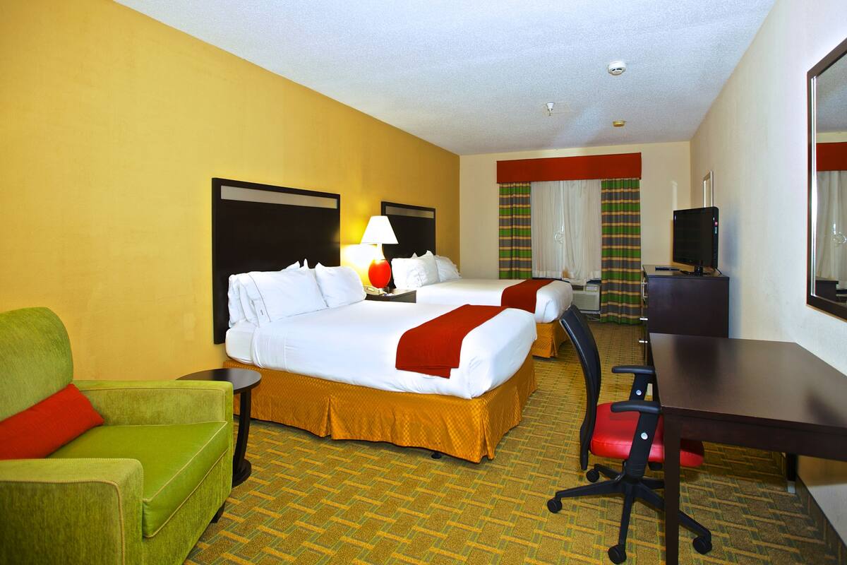 A hotel room with two beds, a desk, a chair, a TV, and a window with curtains.