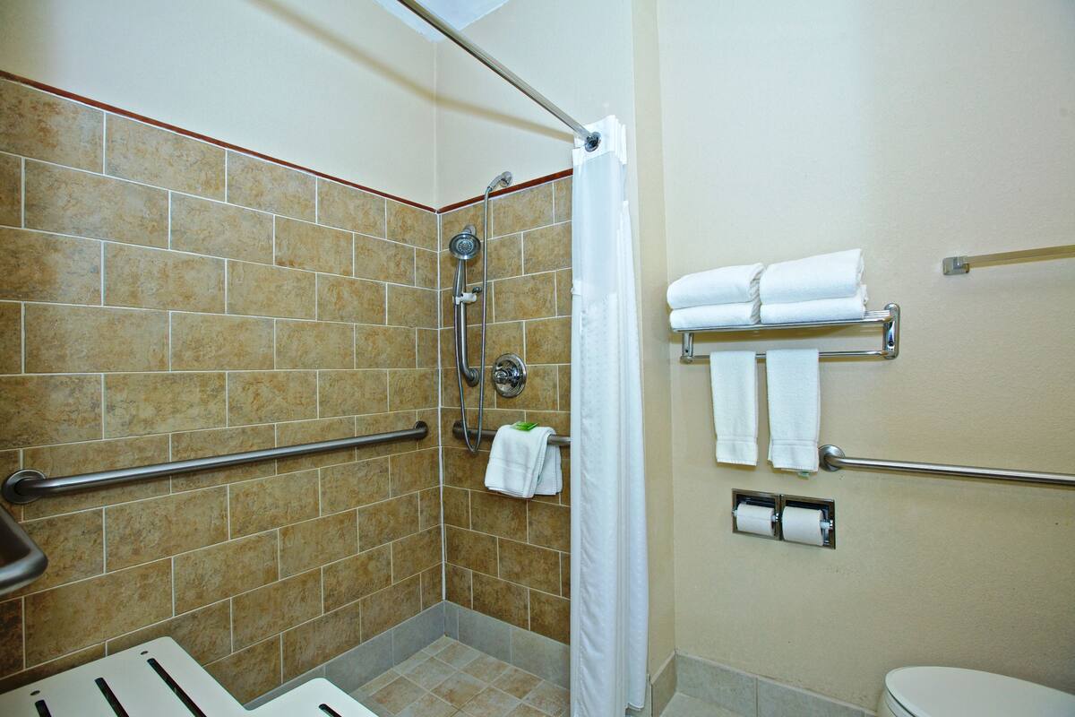 A shower area with a grab bar, a toilet, and a towel rack with towels.