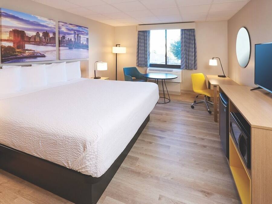 Habitació d'hotel amb un llit gran, una taula de nit, una televisió plana, una cadira i una finestra amb cortines.