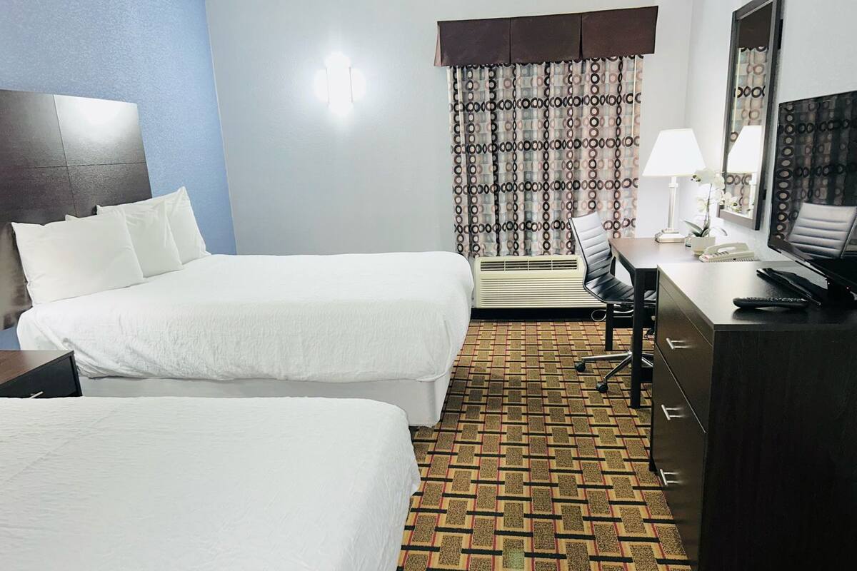 A hotel room with two beds, a desk with a computer, a chair, a lamp, and a large mirror.