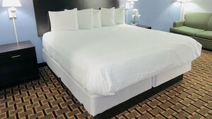 A hotel room with a large bed, two bedside tables with lamps, a green chair, and patterned carpet. - Days Inn by Wyndham Glen Allen/Richmond North (Glen Allen)