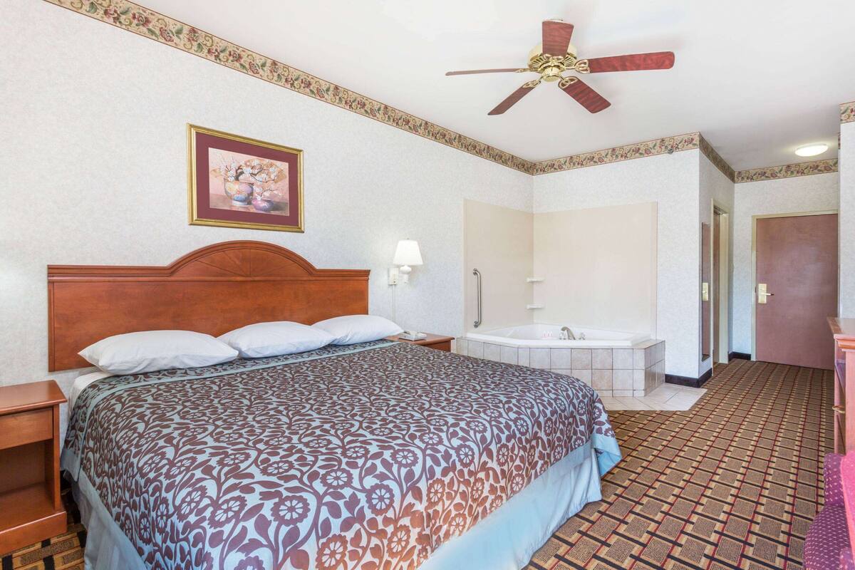 A hotel room with a bed, a ceiling fan, a bathroom with a bathtub, and a door leading to another room.