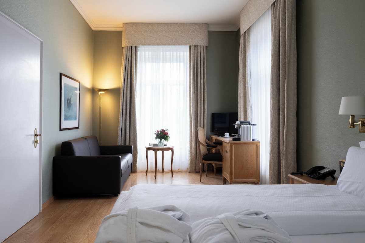 Ett hotellrum med en säng, ett skrivbord, en stol, en tv och ett nattduksbord med en lampa.