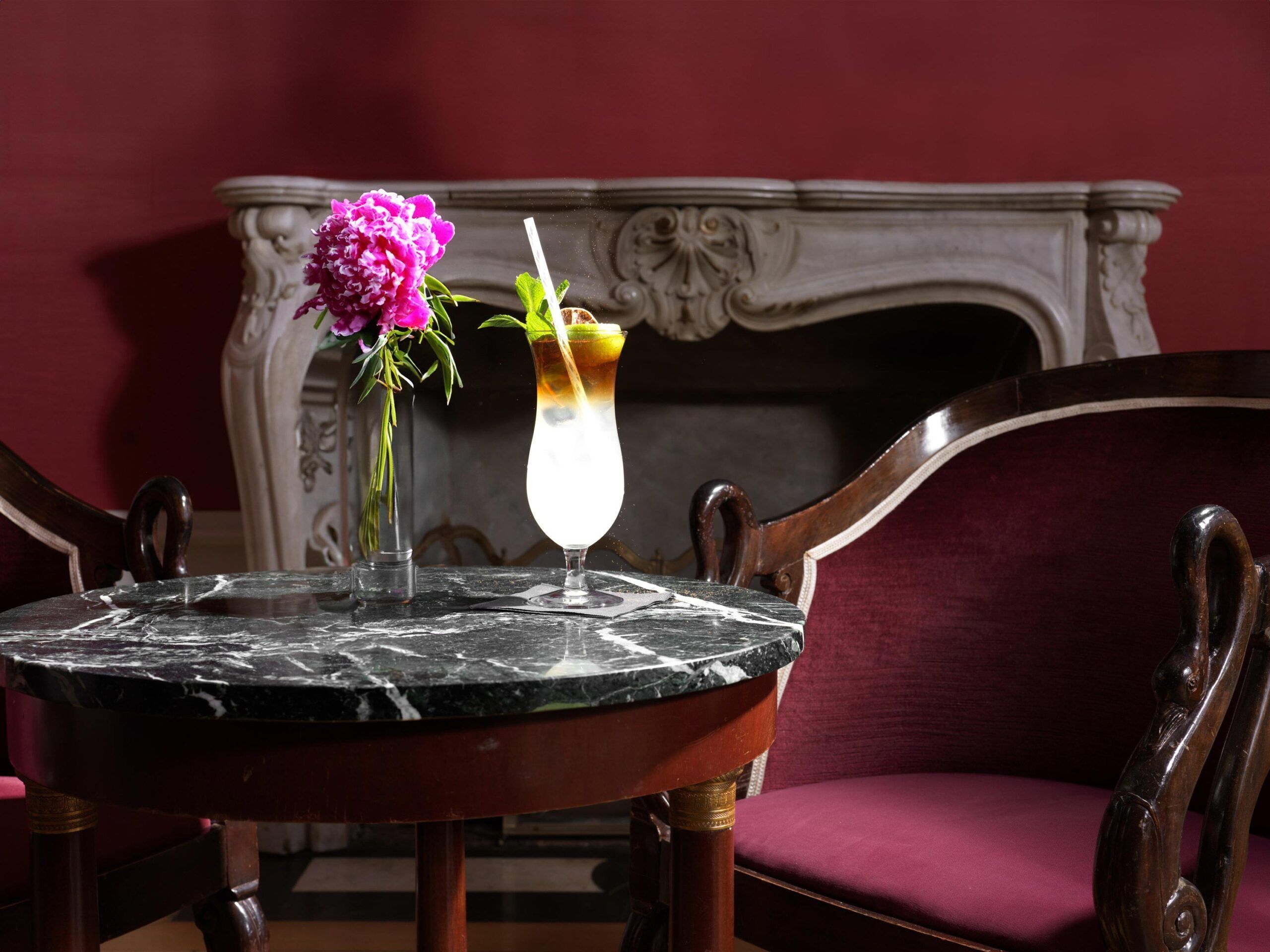 Un tavolo con piano in marmo, un vaso con fiori e un bicchiere da cocktail con una cannuccia.