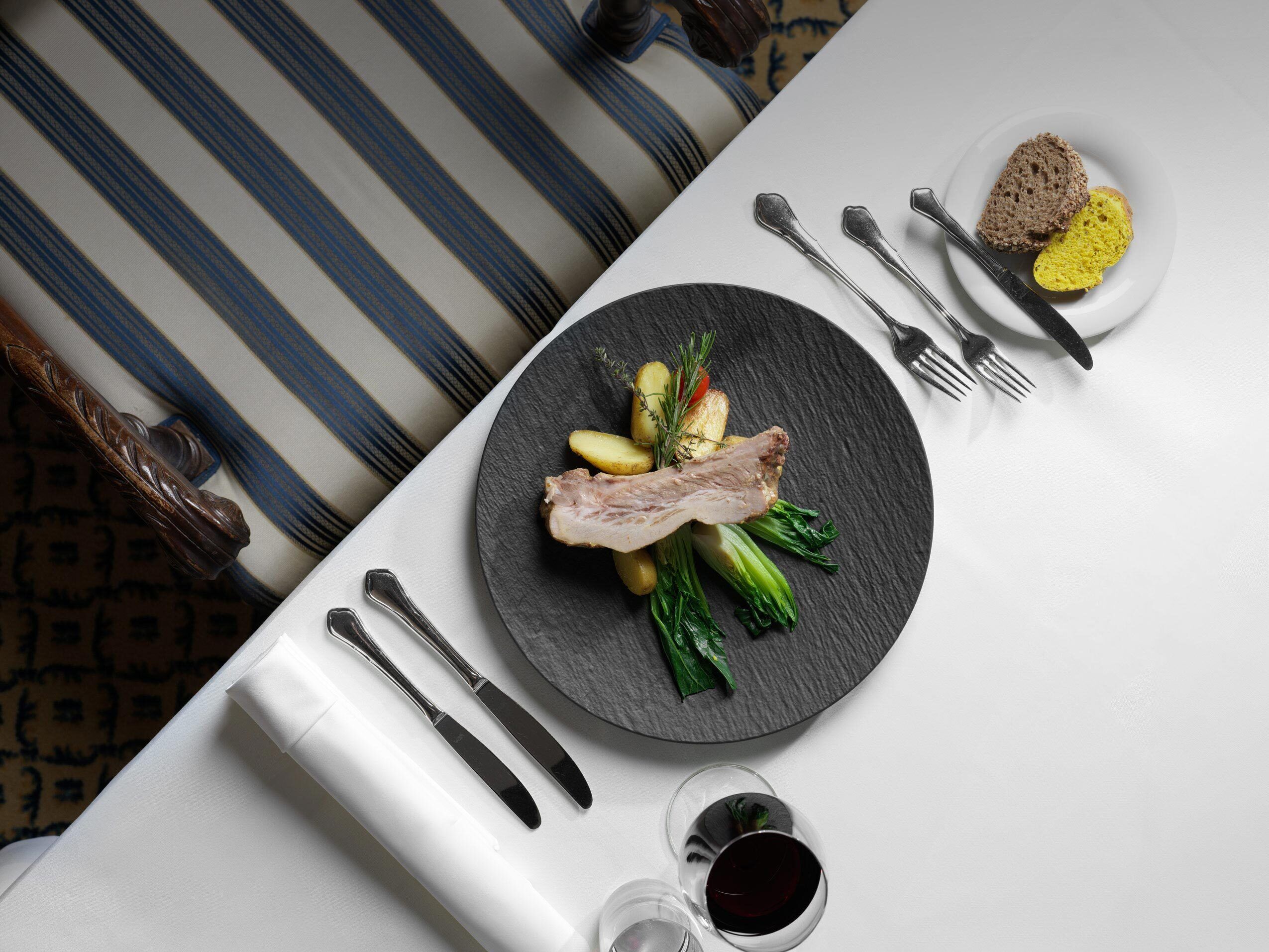 Une table à manger avec une assiette de nourriture, des couverts et un verre de vin rouge.