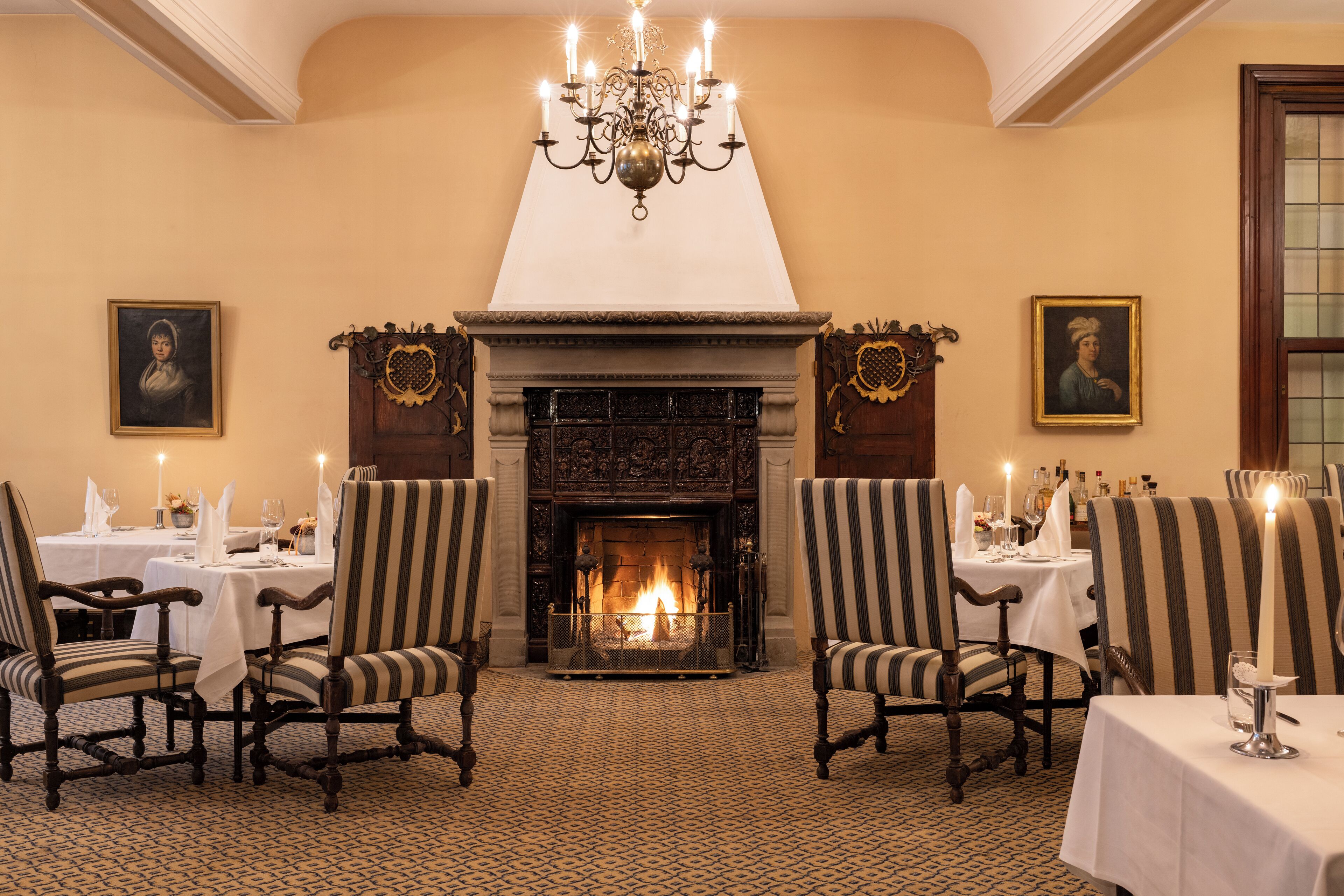 A dining room with a fireplace, striped chairs, and tables set for dining.